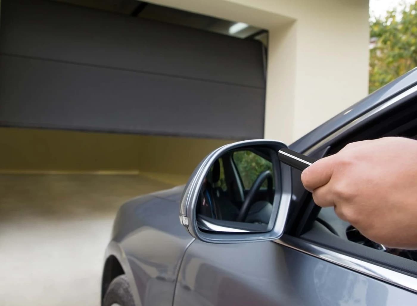 Porte de garage sectionnelle grise en cours d’ouverture, commandée à la télécommande depuis une voiture