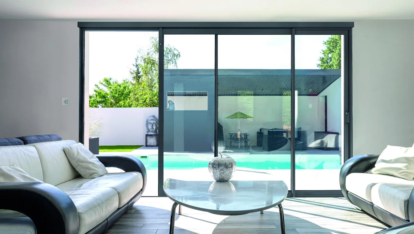 Grande baie coulissante aluminium anthracite à quatre vantaux, vue depuis un séjour, ouverte sur une terrasse et une piscine