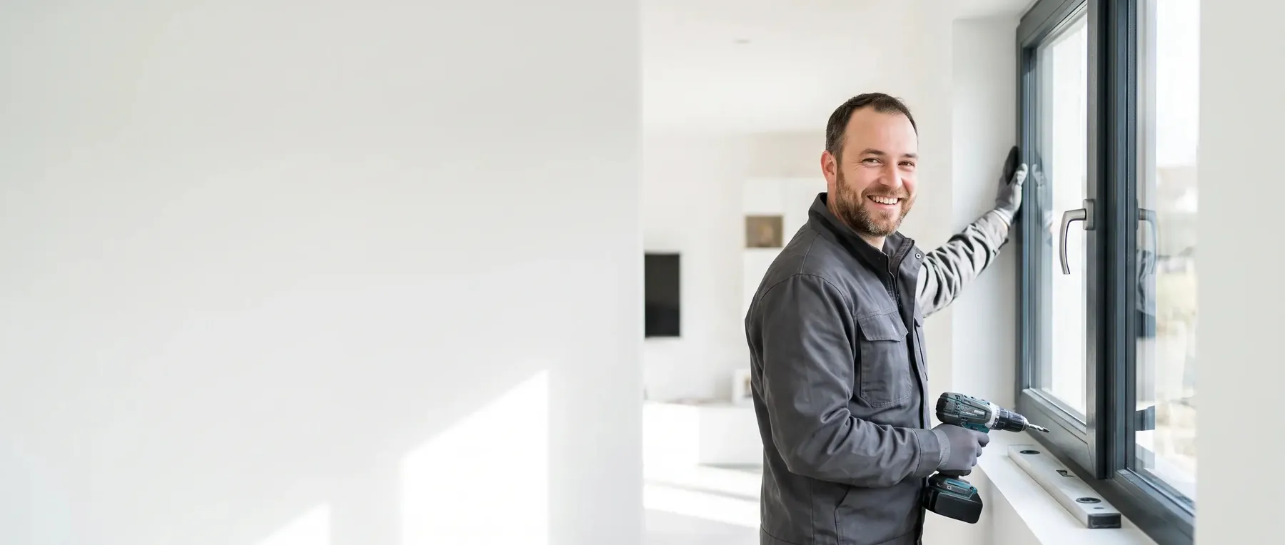 Poseur souriant, perceuse en main, devant une fenêtre aluminium anthracite qu’il vient d’installer