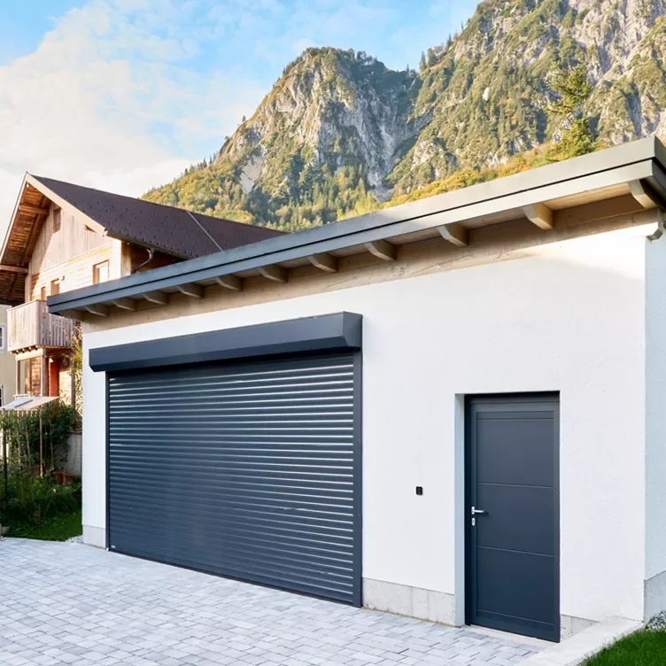 Porte de garage enroulable anthracite avec son coffre en façade, à côté d’une porte de service assortie
