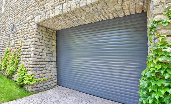 Porte de garage enroulable grise posée dans une baie en pierre