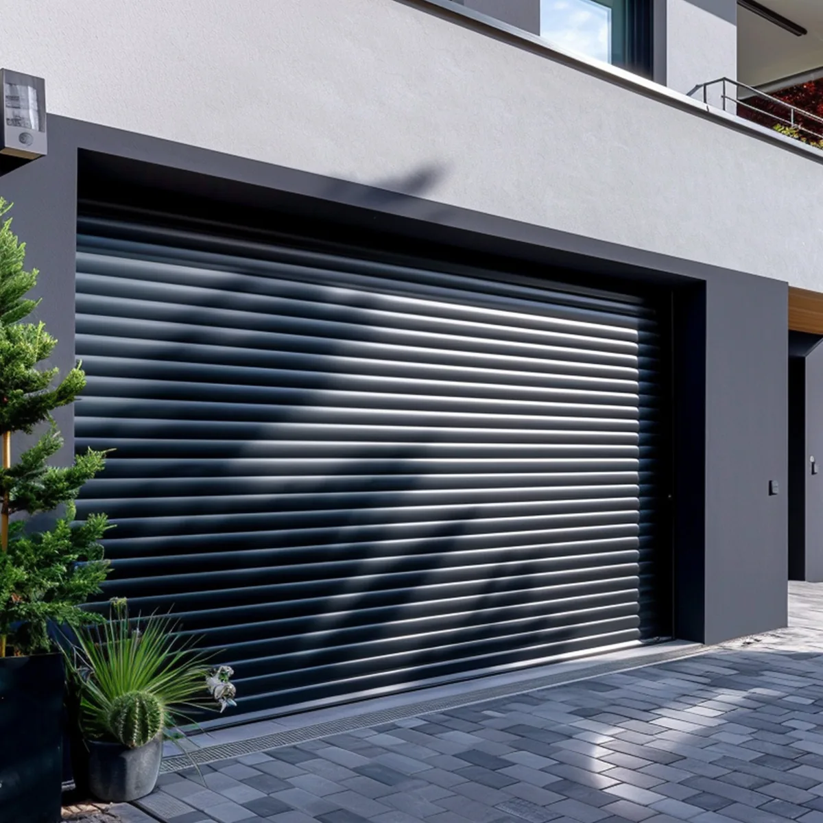 Porte de garage enroulable aluminium anthracite fermée, façade grise et allée pavée