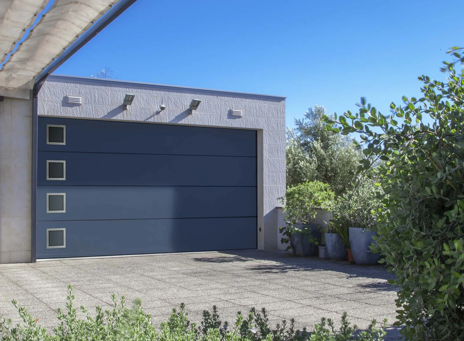Porte de garage sectionnelle gris bleuté à quatre hublots carrés, vue complète sous un ciel bleu