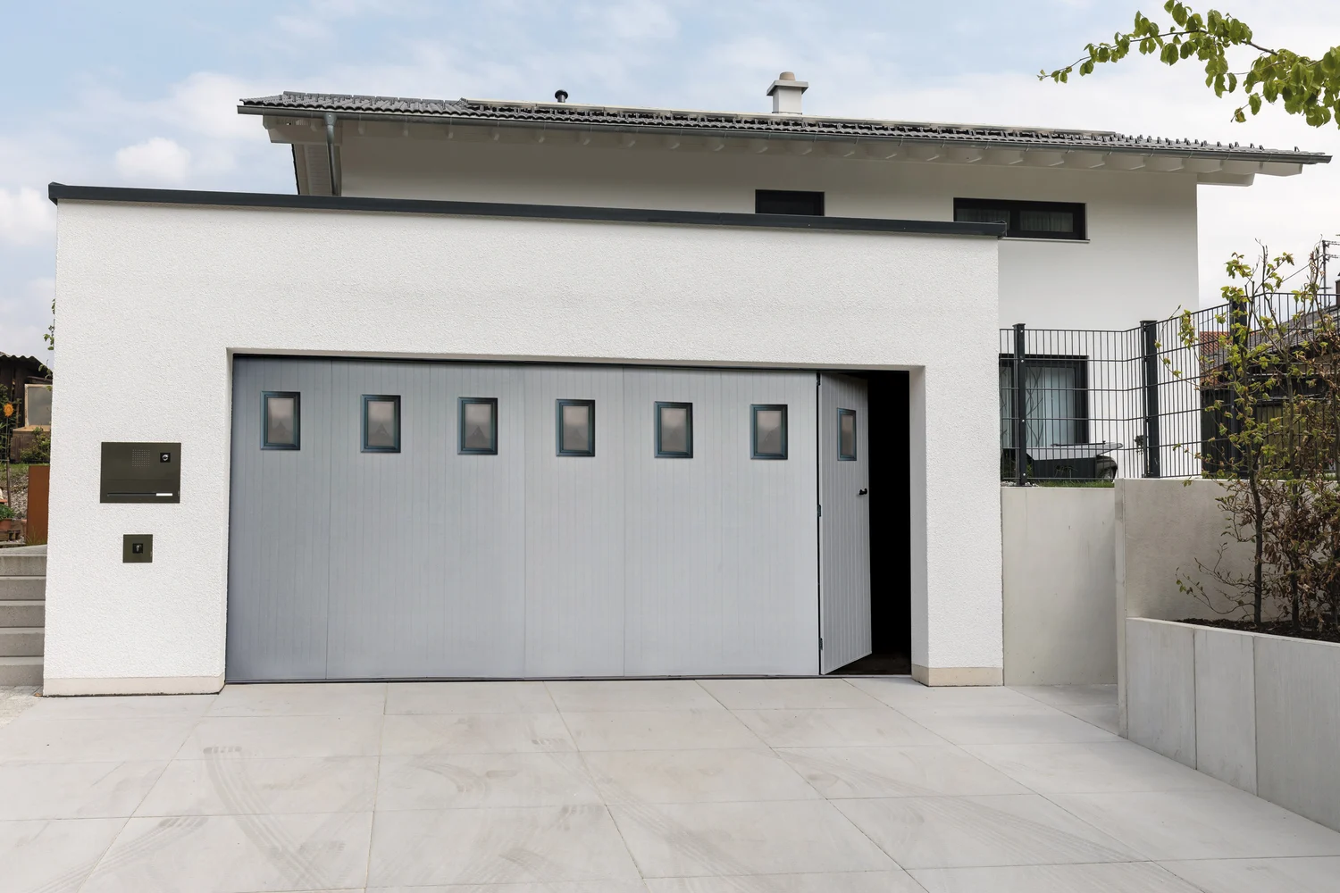 Porte de garage coulissante PVC avec hublots dans une façade contemporaine