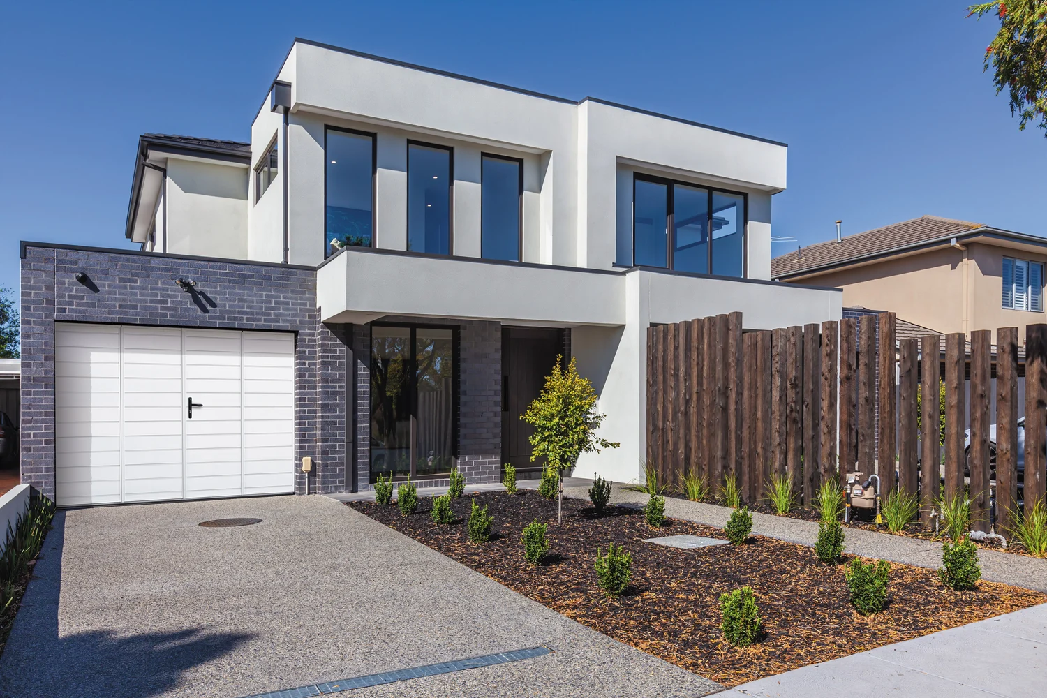 Porte de garage à la française aluminium blanche à plusieurs vantaux dans une façade de maison